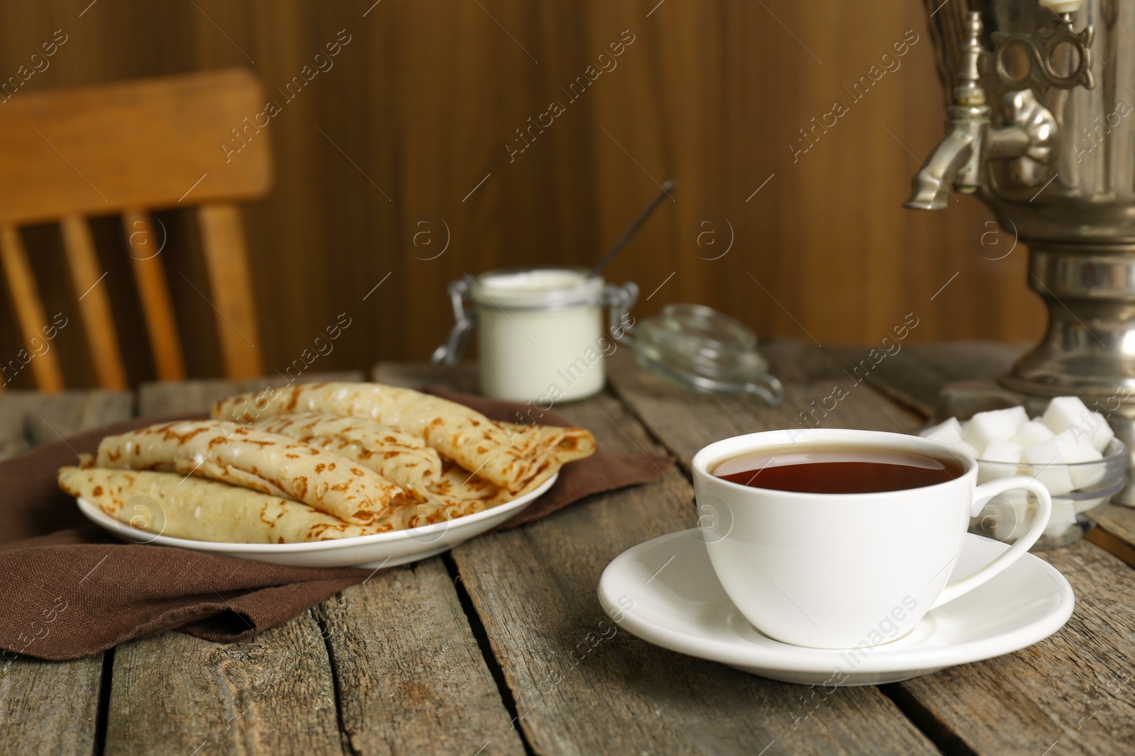 Photo of Vintage samovar, cup of hot drink and pancakes served on wooden table. Traditional Russian tea ceremony