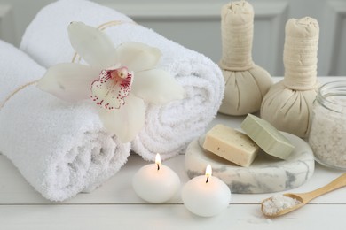 Photo of Beautiful spa composition. Towels, herbal bags, soap bars and burning candles on white wooden table