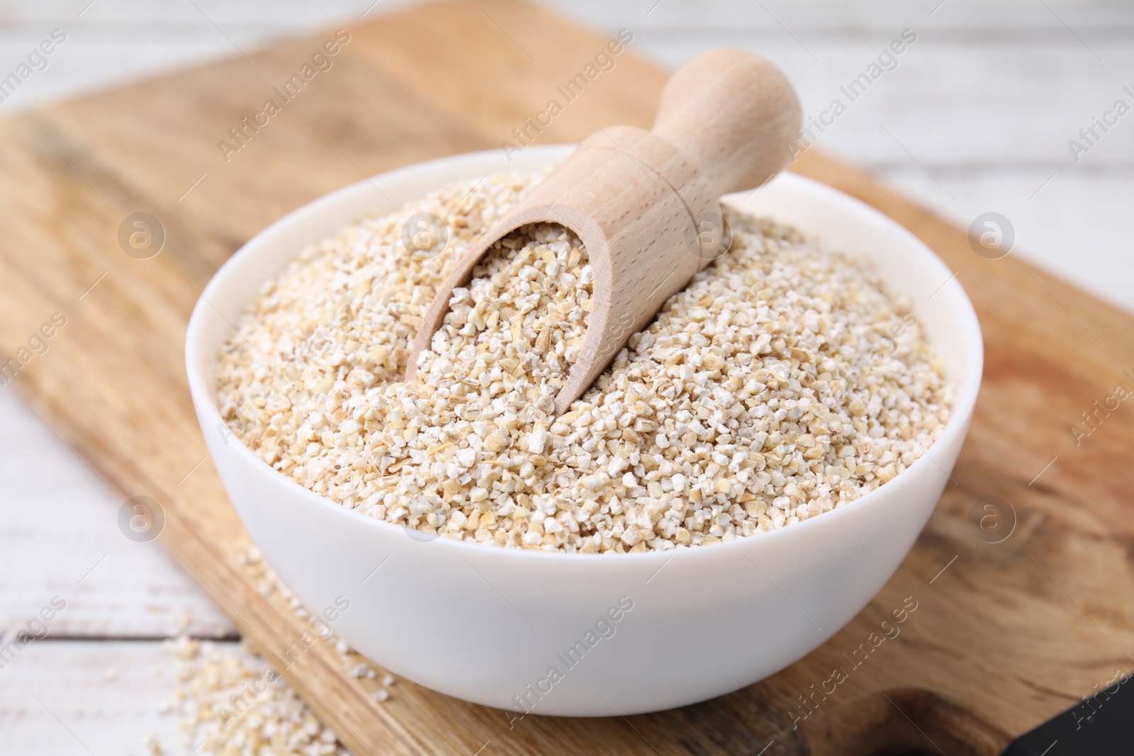 Photo of Raw barley groats and scoop in bowl on white wooden table, closeup