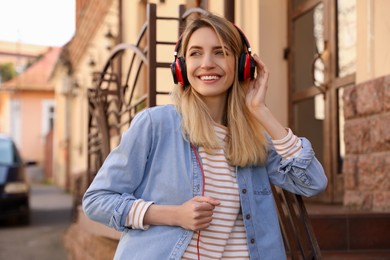 Photo of Happy young woman with headphones listening to music on city street