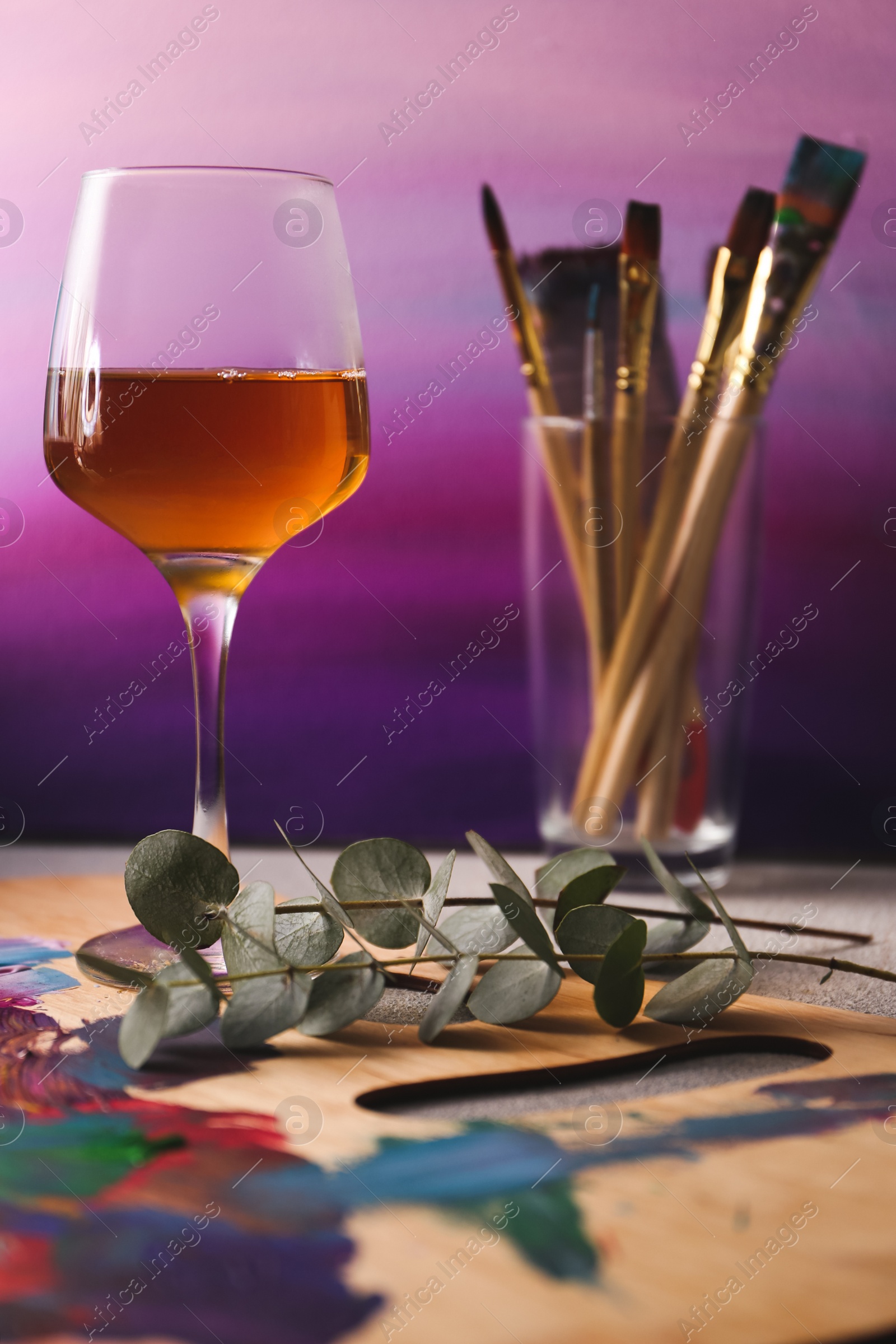 Photo of Wooden artist's palette with colorful paints and glass of wine on grey table