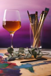 Wooden artist's palette with colorful paints and glass of wine on grey table