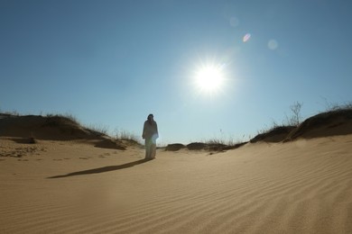 Photo of Man in arabic clothes walking through desert on sunny day, back view