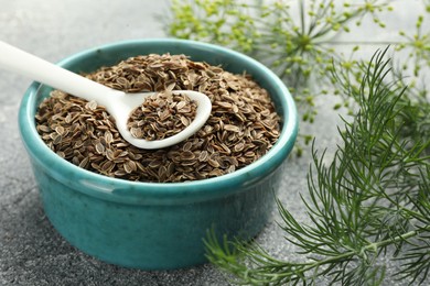 Bowl of dry seeds, spoon and fresh dill on grey table, closeup