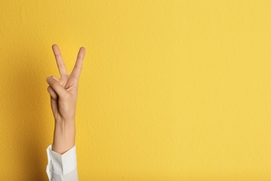 Photo of Young woman showing victory gesture on color background. Space for text