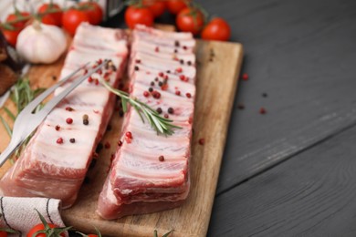 Photo of Raw pork ribs with peppercorns and rosemary on grey wooden table. Space for text