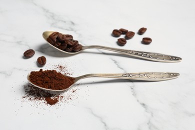 Spoons of ground coffee and beans on white marble table