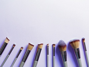 Photo of Many different makeup brushes on lilac background, flat lay. Space for text