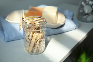 Photo of Many wooden clothespins in glass jar on white table, space for text