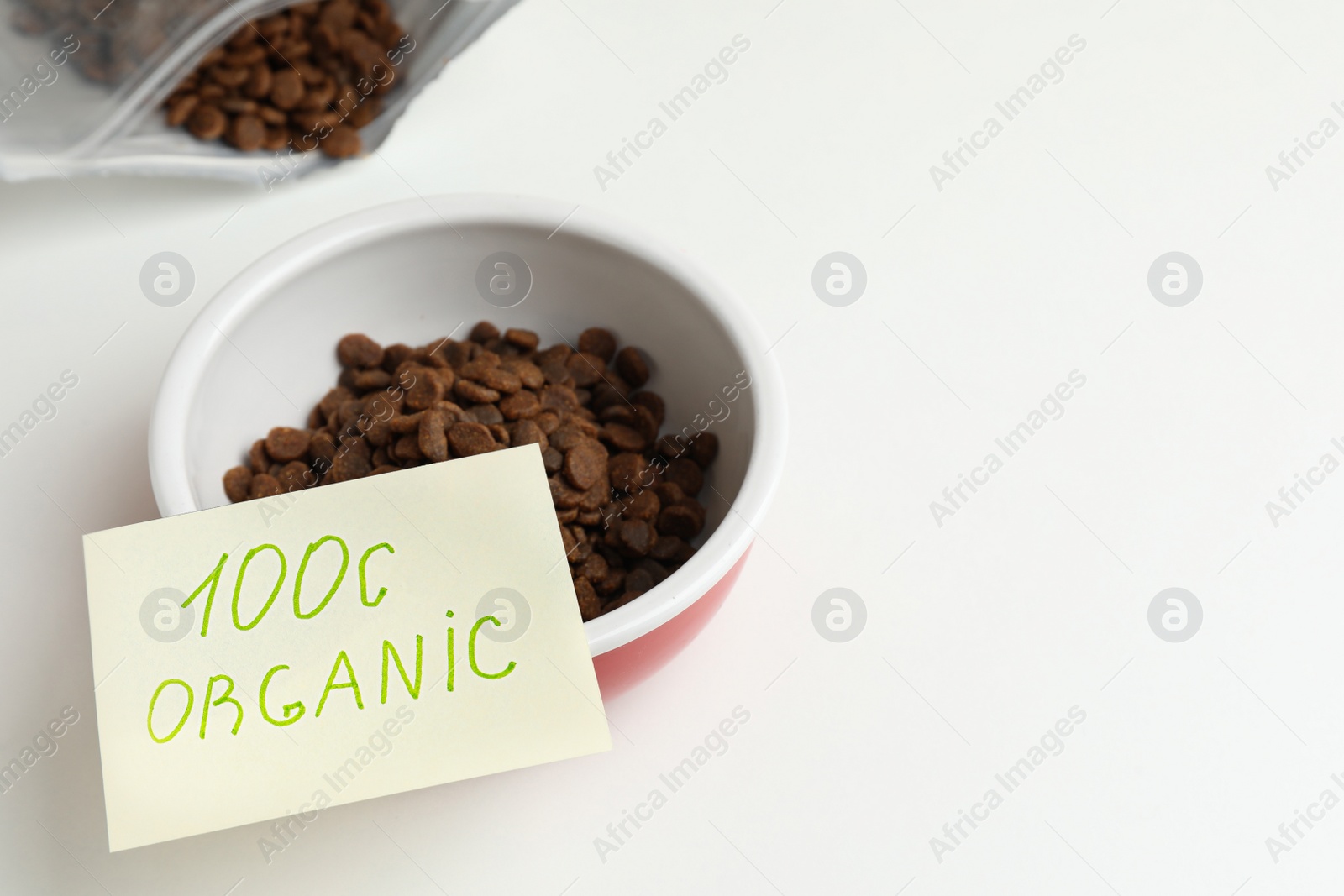 Photo of Pack and feeding bowl of dry cat food with note 100% Organic on white table. Space for text