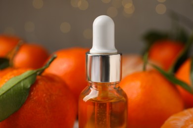 Photo of Bottle of tangerine essential oil and fresh fruits on blurred background, closeup
