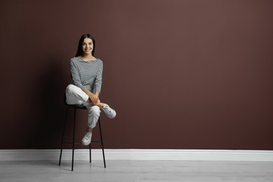 Photo of Beautiful young woman sitting on stool near brown wall. Space for text
