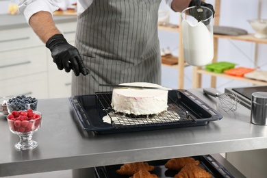 Male pastry chef preparing cake at table in kitchen, closeup