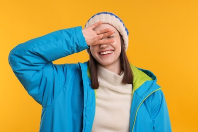 Photo of Beautiful woman covering eyes and smiling on orange background