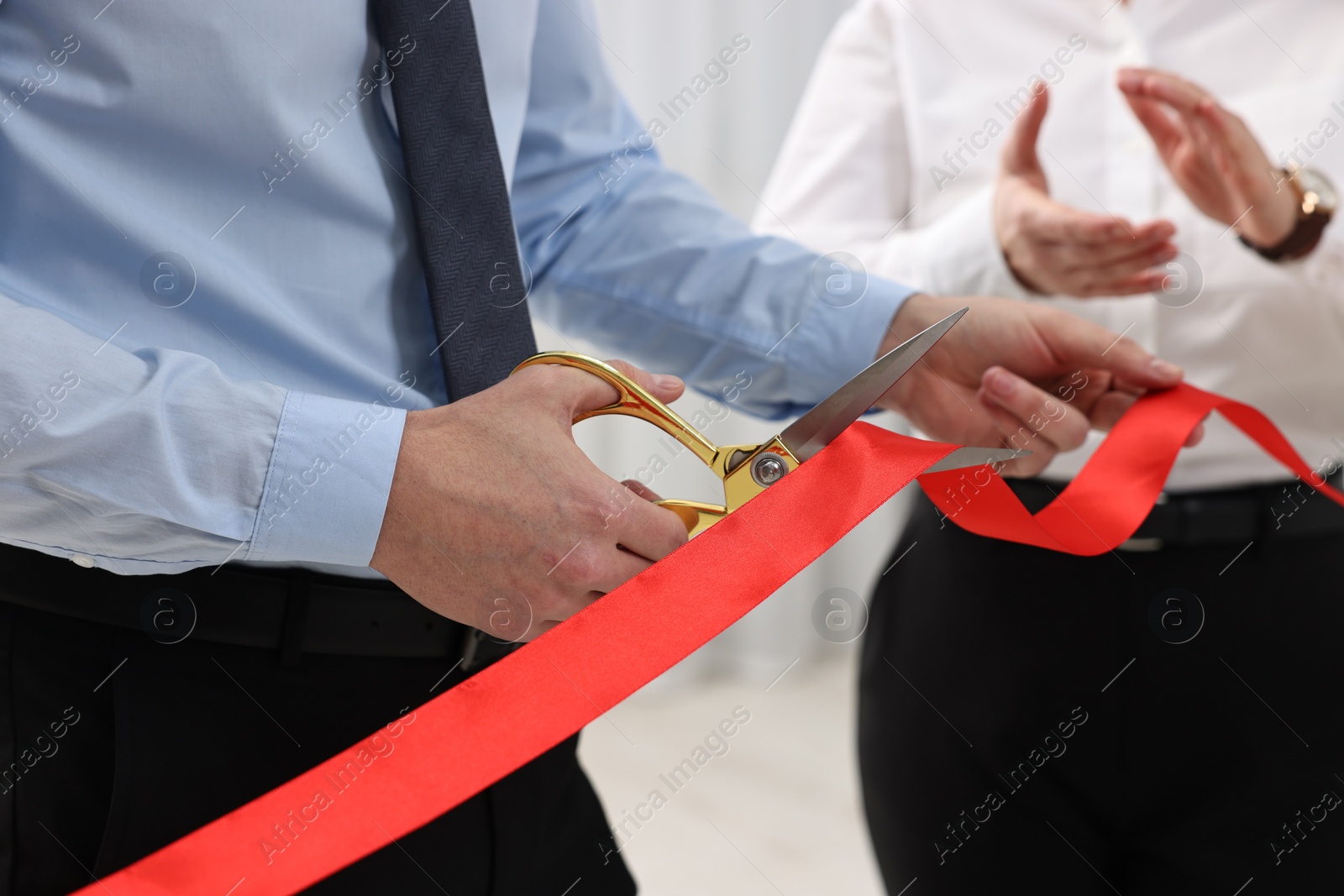 Photo of Man cutting red ribbon with scissors on blurred background, closeup