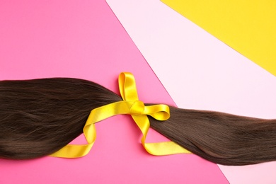 Photo of Brown hair tied with ribbon and space for text on color background, top view