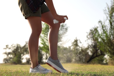 Photo of Woman applying insect repellent onto leg in park, closeup. Space for text