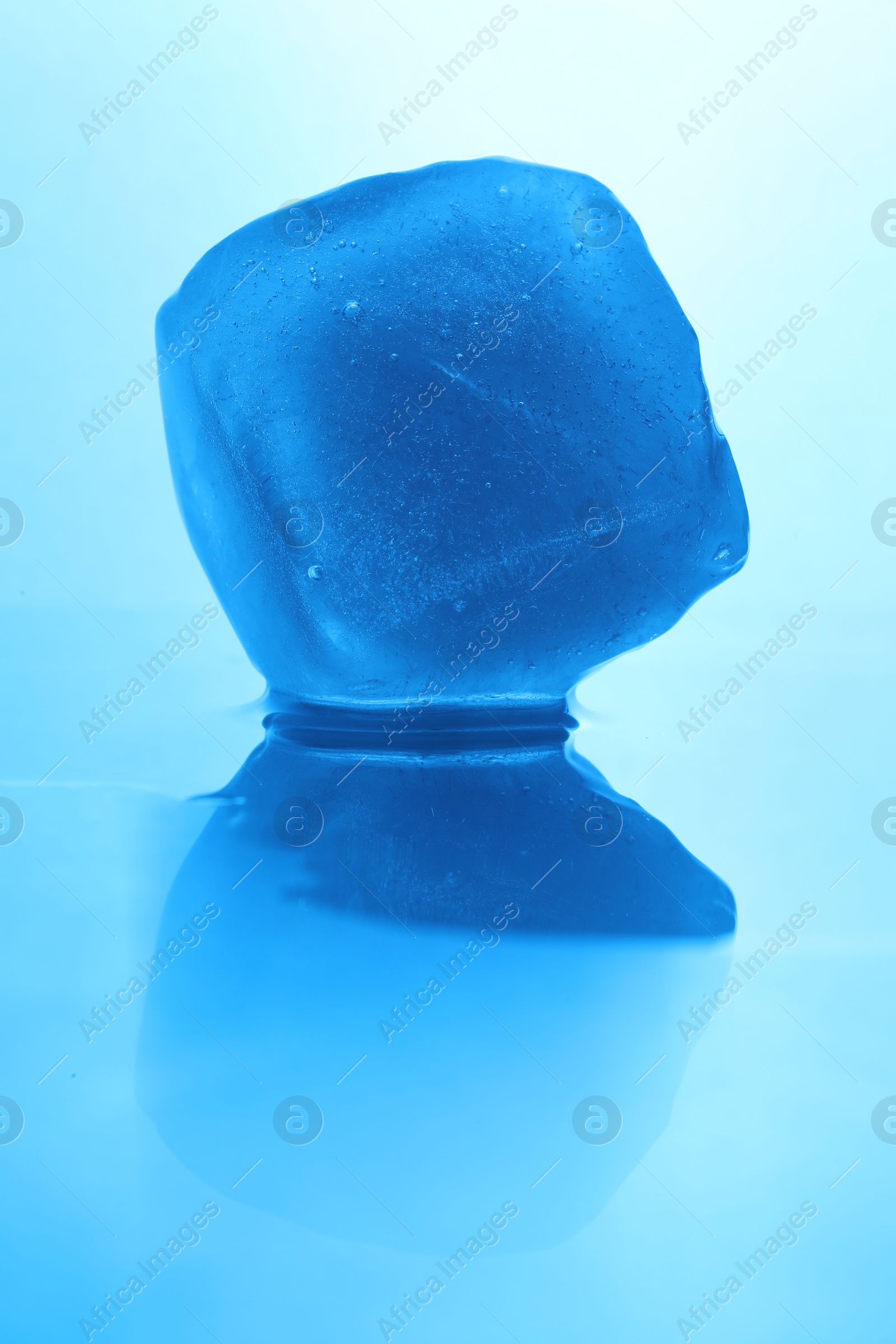 Photo of Crystal clear ice cube on light blue background, closeup. Color tone effect