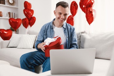 Photo of Valentine's day celebration in long distance relationship. Man opening gift from his girlfriend at home
