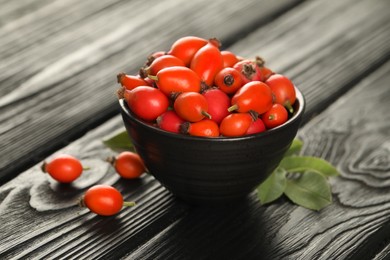 Photo of Ripe rose hip berries with green leaves on black wooden table