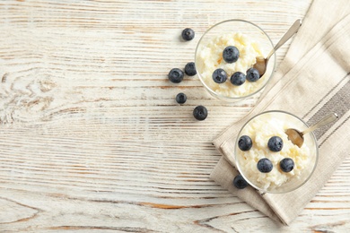 Photo of Creamy rice pudding with blueberries in dessert bowls on white wooden table, top view. Space for text
