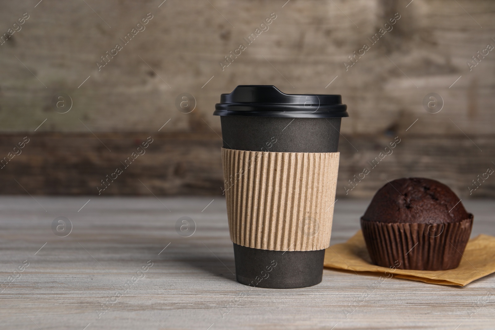 Photo of Paper cup with black lid and muffin on wooden table, space for text. Coffee to go