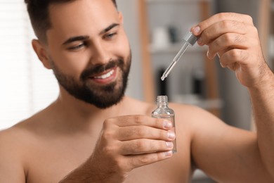 Photo of Handsome man with cosmetic serum in his hands indoors, selective focus