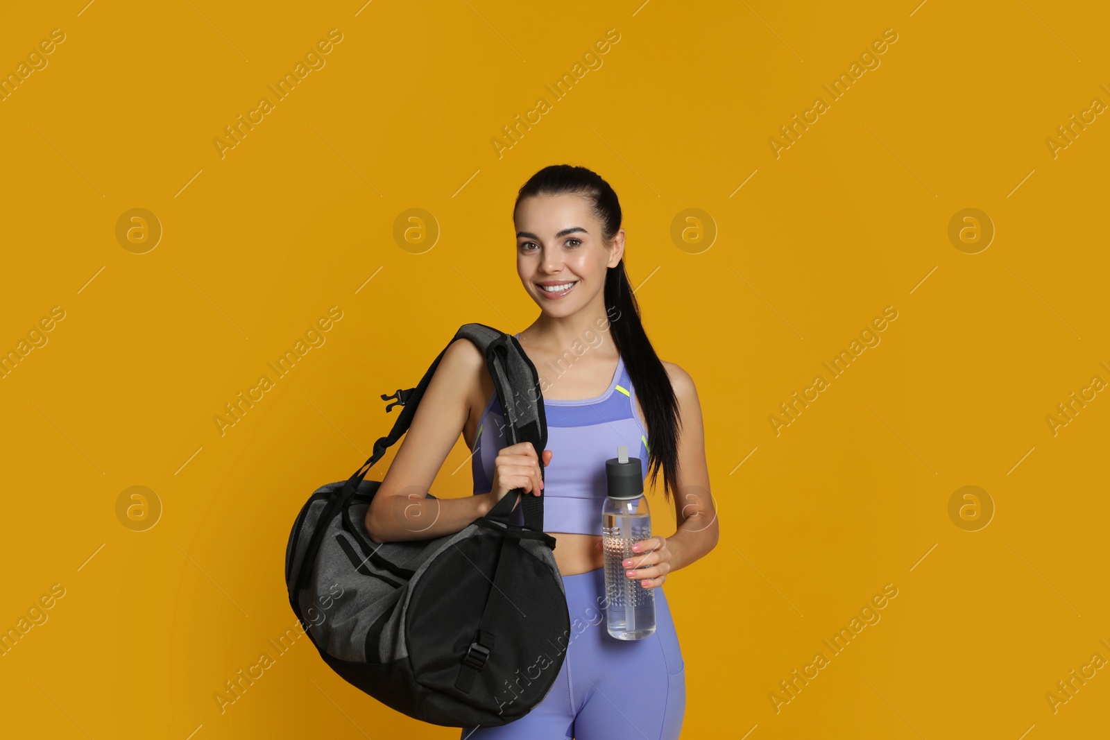 Photo of Beautiful woman with sports bag and bottle of water on yellow background