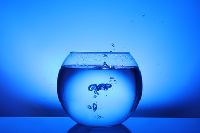 Photo of Splash of water in round fish bowl on blue background