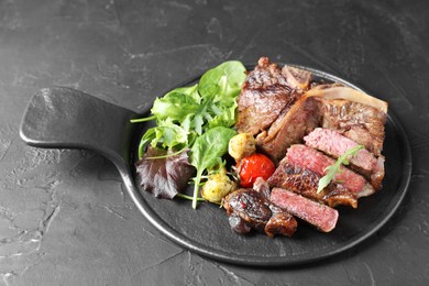 Photo of Delicious grilled beef meat, vegetables and greens on black table