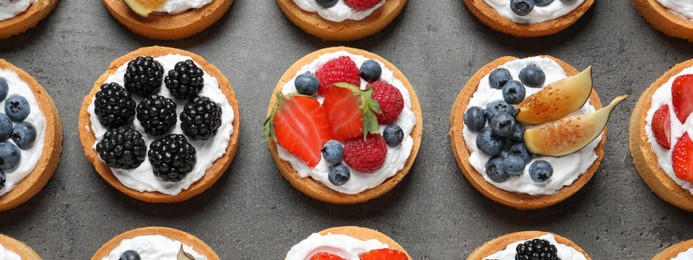 Image of Delicious tartlets with fresh berries on grey table, flat lay. Banner design