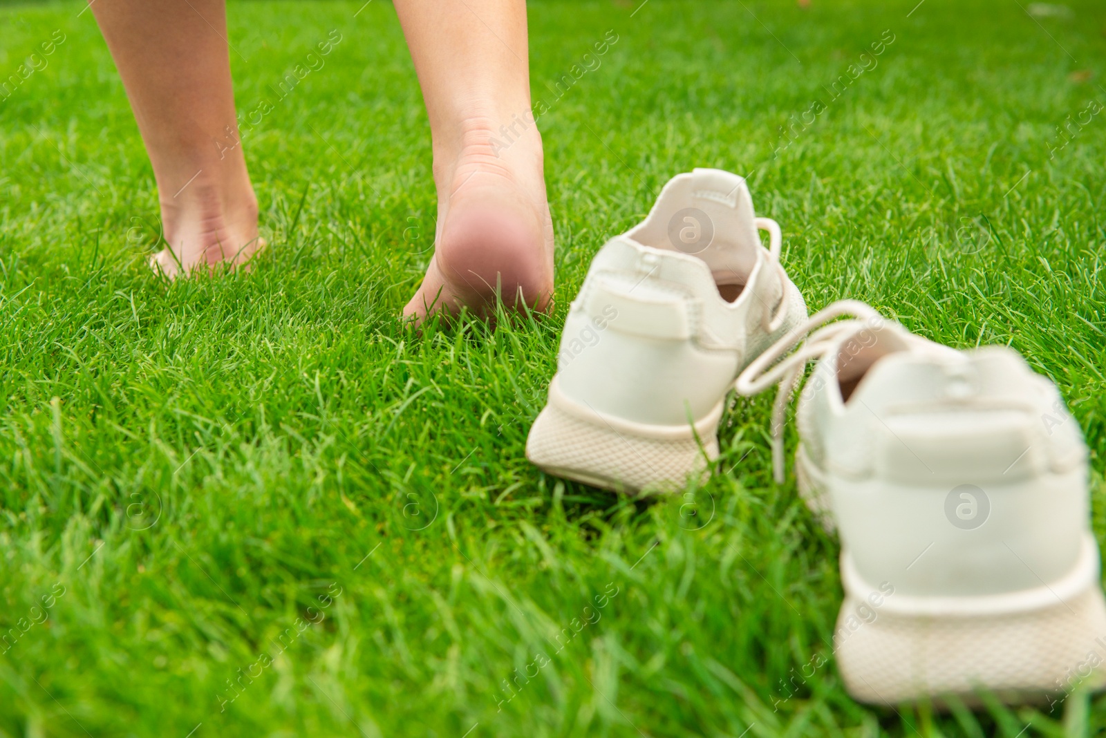 Photo of Woman leaving her sneakers and walking away barefoot on green grass, closeup