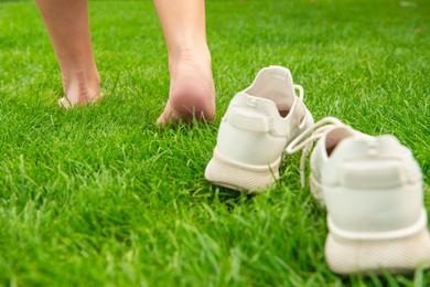 Woman leaving her sneakers and walking away barefoot on green grass, closeup