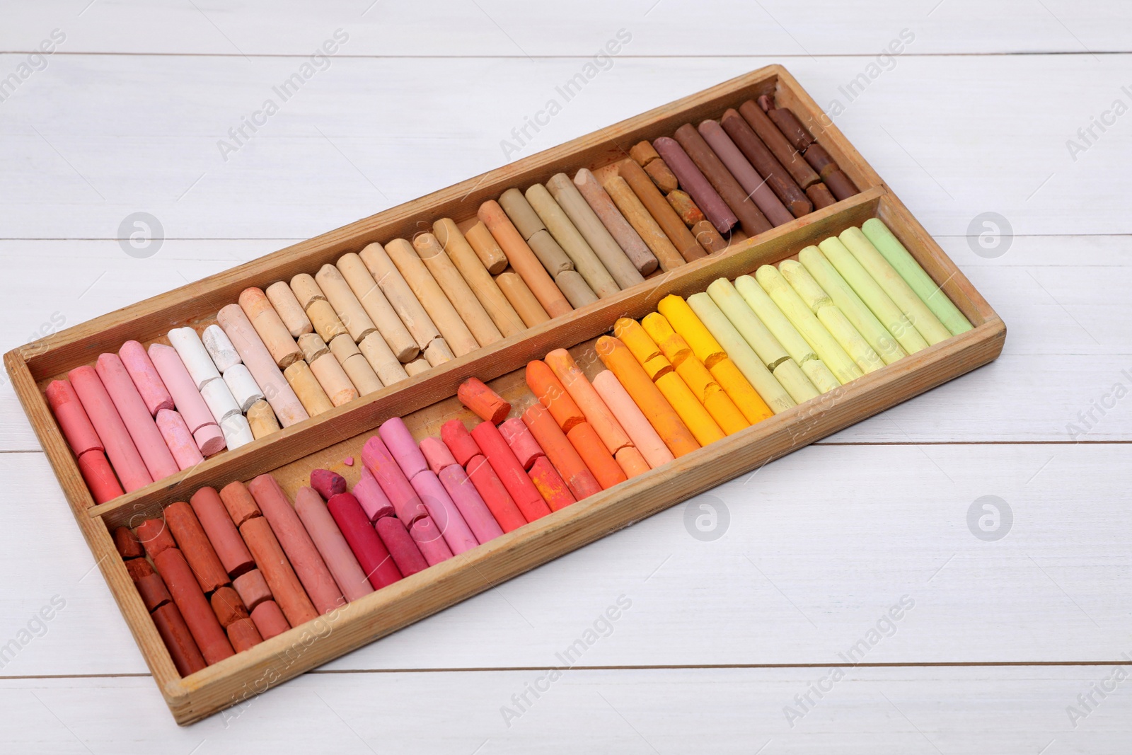 Photo of Set of soft pastels in box on white wooden table. Drawing material