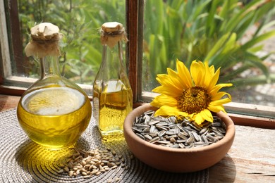 Bottles of sunflower oil, seeds and flower on wooden table indoors