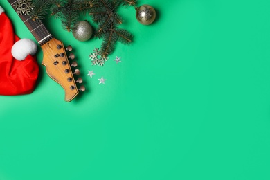 Photo of Christmas music. Flat lay composition with guitar and Santa hat on green background, space for text