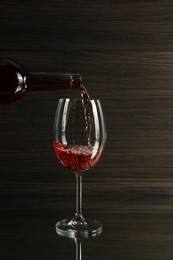 Photo of Pouring rose wine from bottle into glass on table against wooden background