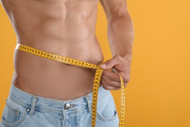 Photo of Shirtless man with slim body and measuring tape around his waist on yellow background, closeup