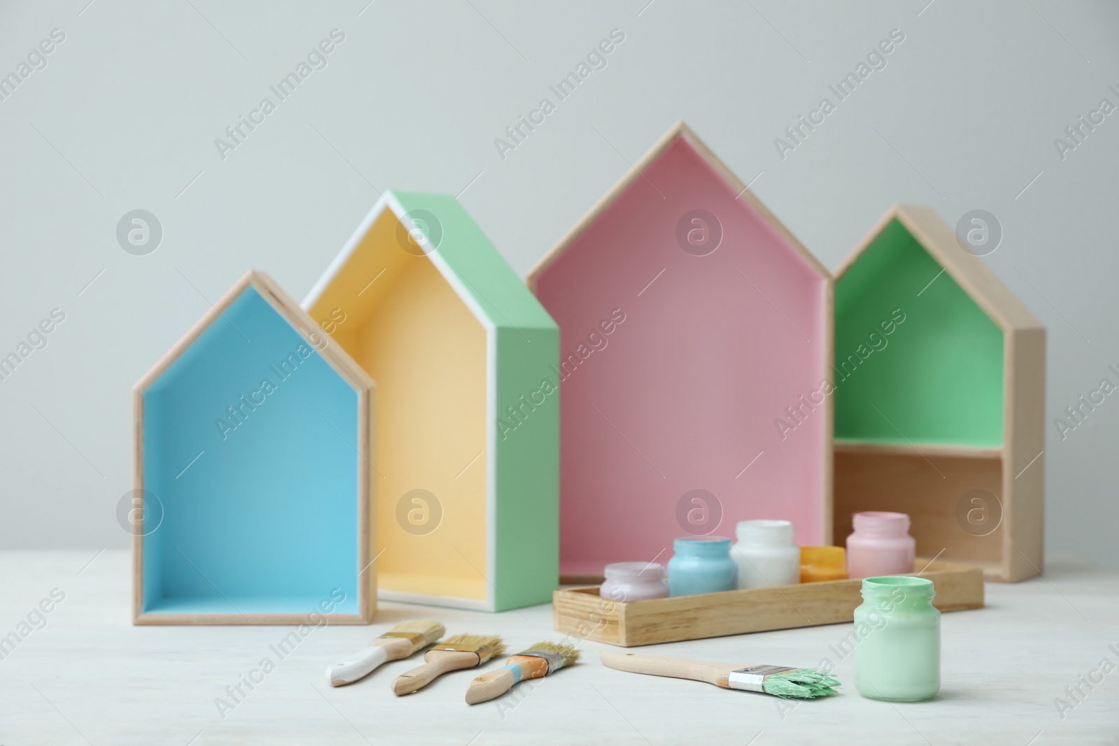 Photo of House shaped shelves, jars of paints and brushes on white table. Interior elements