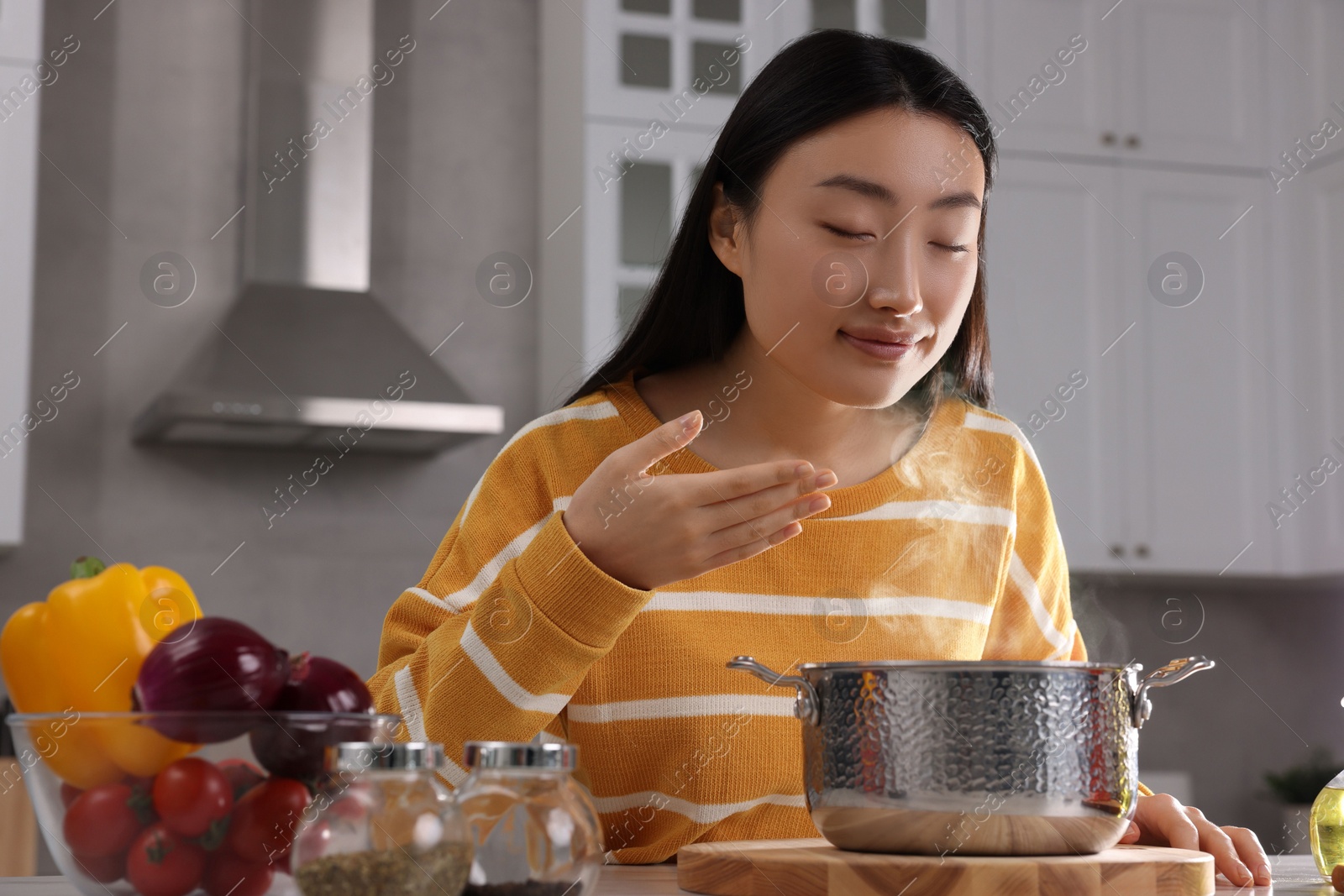 Photo of Beautiful woman smelling soup after cooking at countertop in kitchen