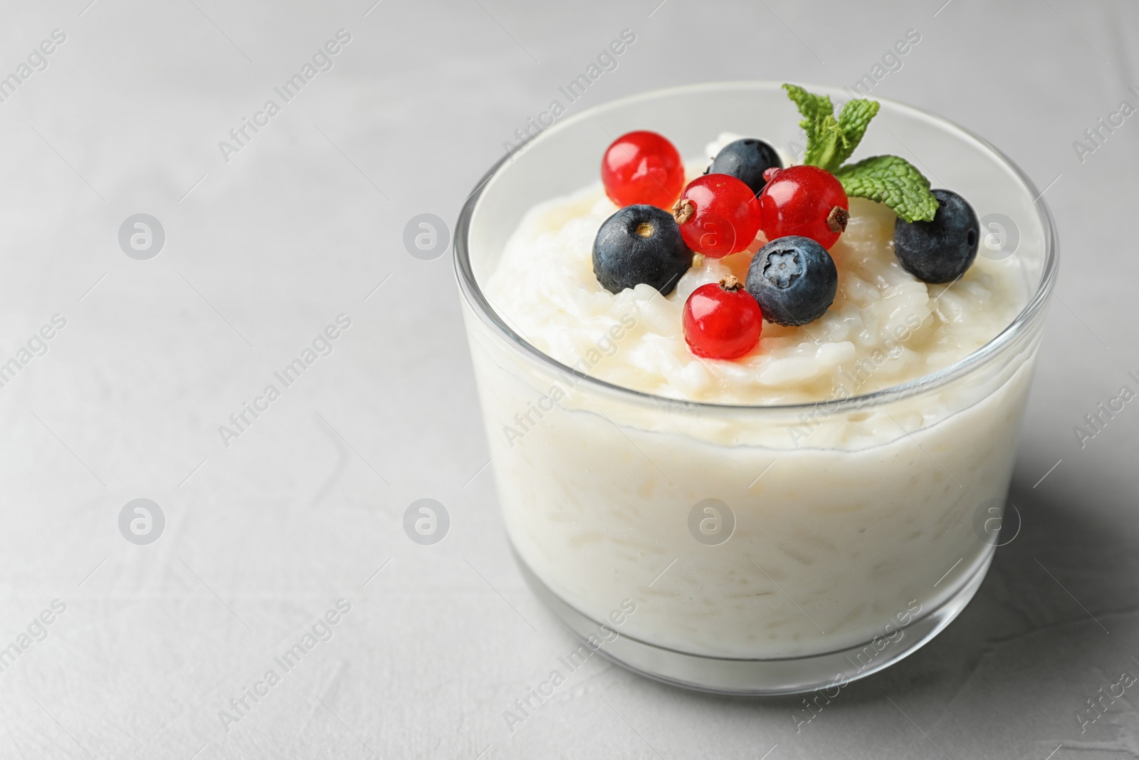 Photo of Delicious rice pudding with berries on light table, closeup. Space for text