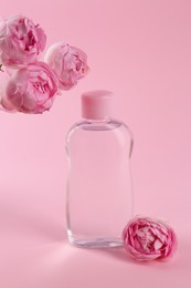 Photo of Bottle with baby oil and beautiful flowers on pink background. Space for text