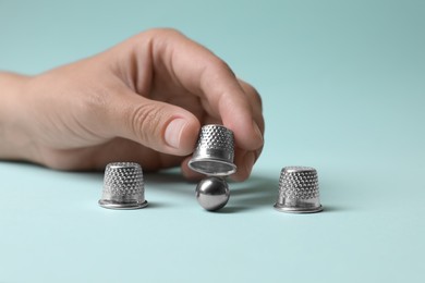 Woman showing metal ball under thimble on light blue background, closeup. Thimblerig game