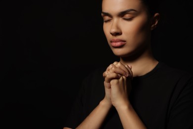 African American woman with clasped hands praying to God on black background. Space for text