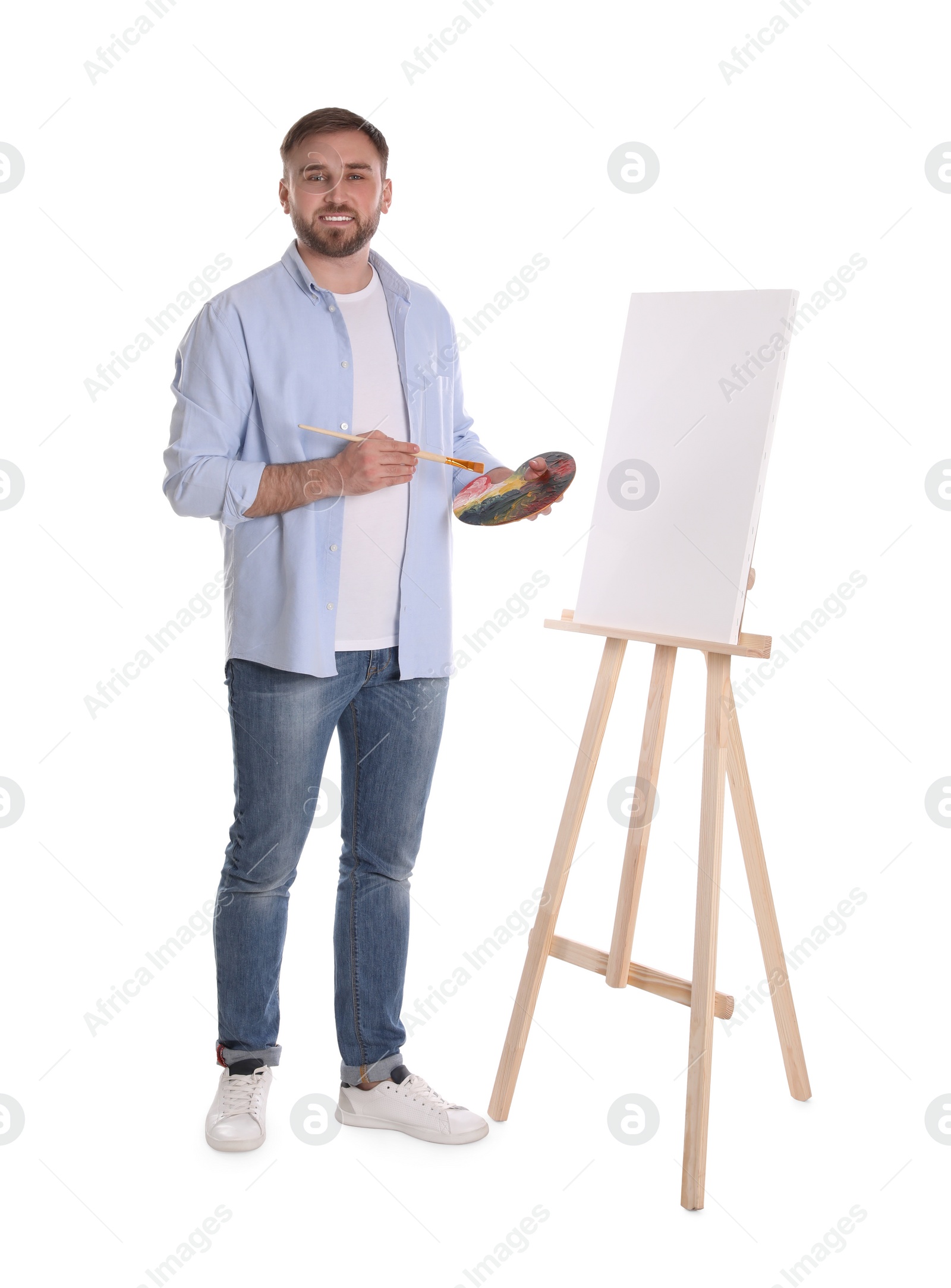 Photo of Man with painting tools near easel on white background. Young artist