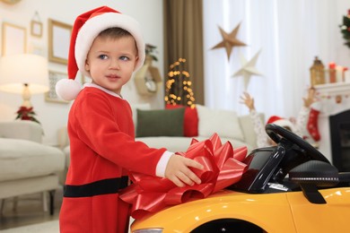 Cute little boy near toy car with big red bow in room decorated for Christmas