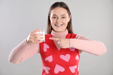 Photo of Happy woman with milk mustache pointing at glass of drink on light grey background
