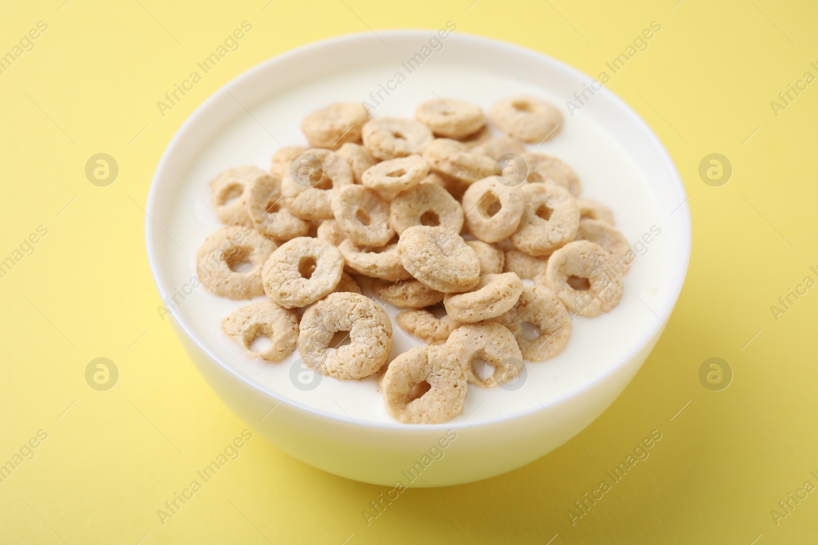 Photo of Breakfast cereal. Tasty corn rings with milk in bowl on yellow background, closeup