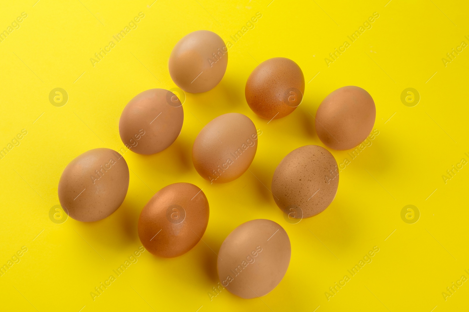 Photo of Raw chicken eggs on yellow background, above view