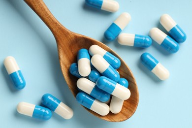 Photo of Antibiotic pills and spoon on light blue background, top view